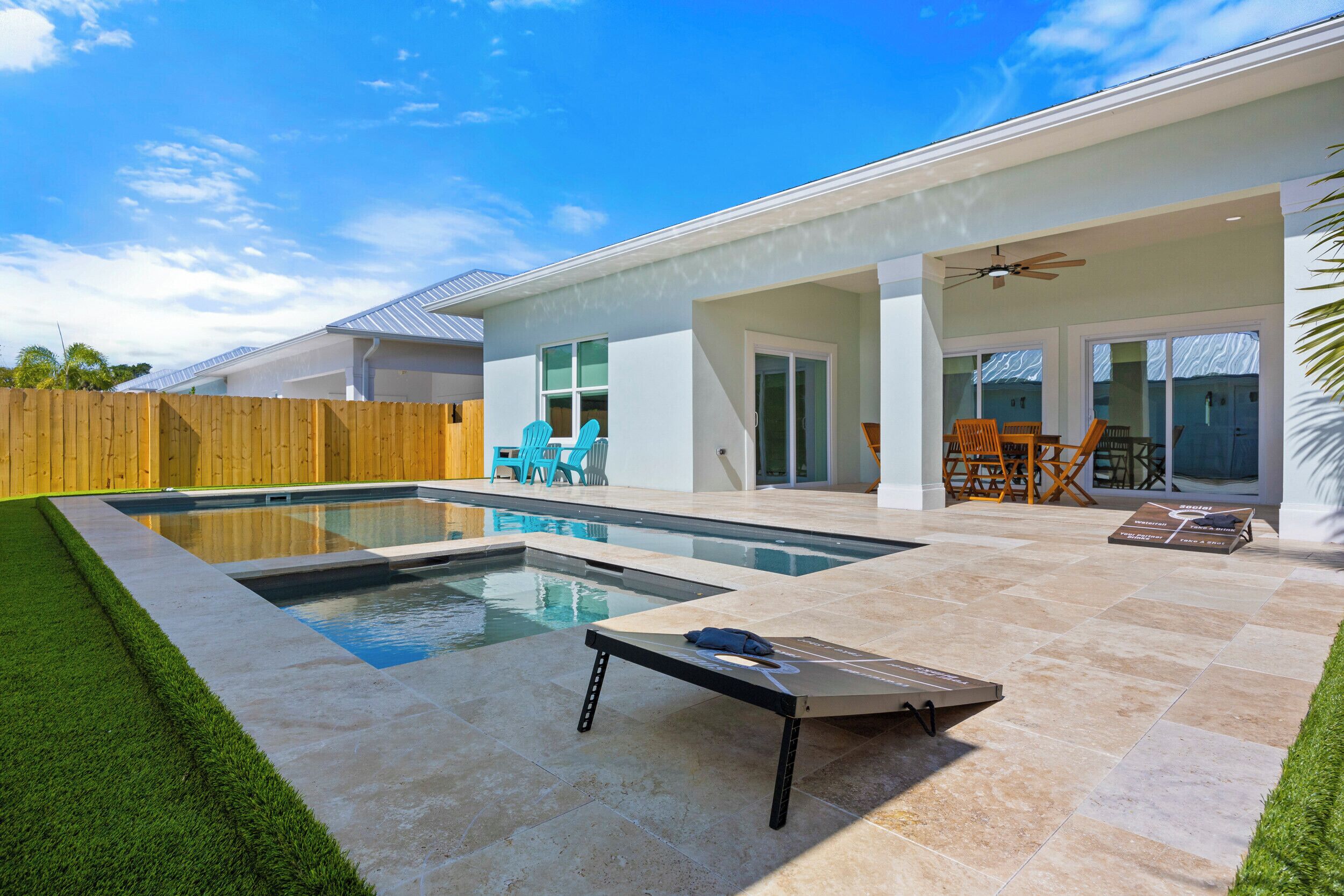 Ein moderner Poolbereich im Freien mit Liegestuhl, Holzzaun und Terrasse mit Stühlen und Tisch.