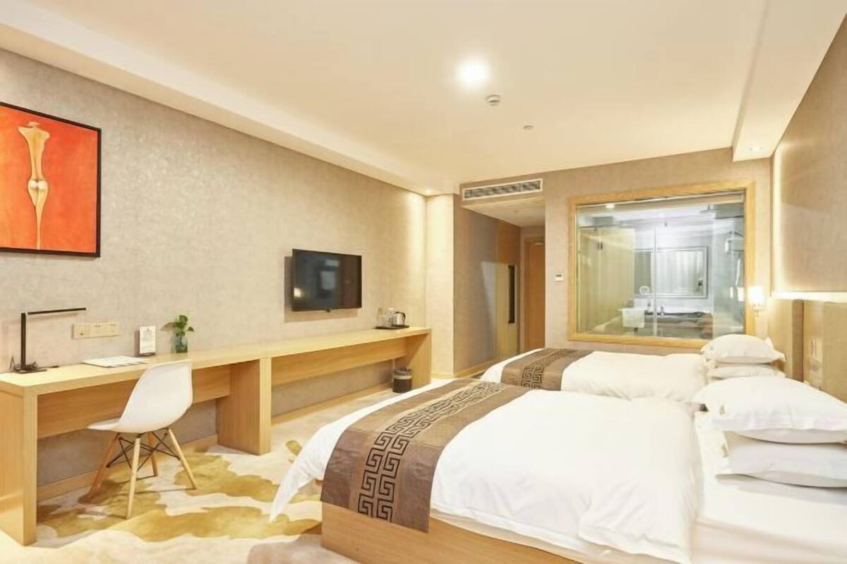 Una habitació d'hotel amb un llit, un escriptori, una cadira, un televisor i un mirall.