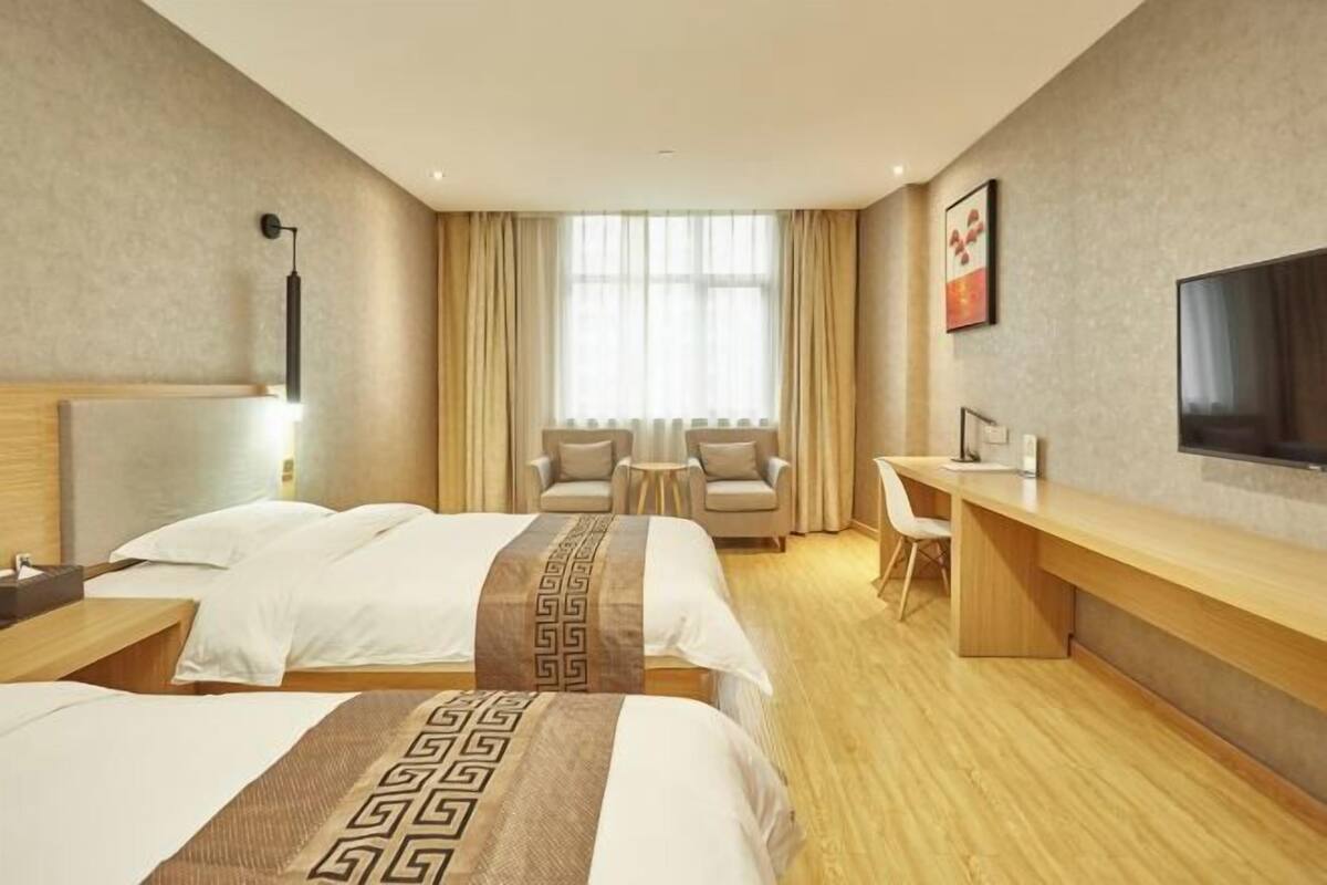 Habitació d'hotel amb dos llits, una taula de treball, una cadira, un televisor i una finestra amb cortines.