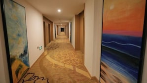 A hotel hallway with a carpeted floor, artwork on the walls, and doors leading to rooms.