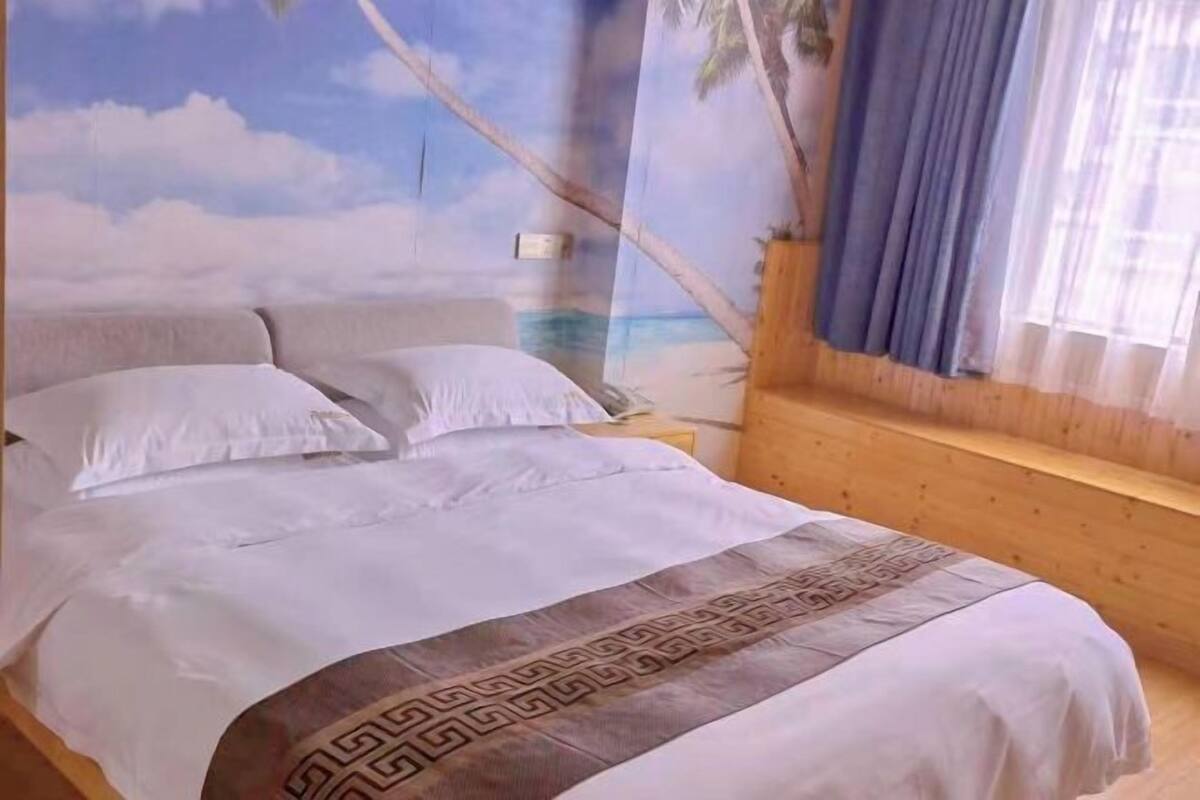 Un llit amb roba blanca i un capçal decoratiu, una banca de fusta i un mural amb una escena de platja.