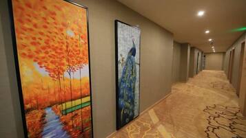 Un pasillo con dos pinturas grandes en las paredes, suelo alfombrado y una serie de puertas a lo largo del corredor.