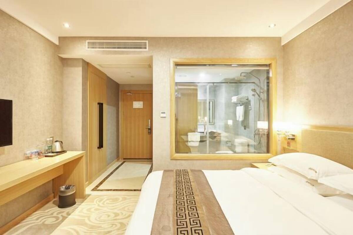 Una habitació d'hotel amb un llit, una taula de nit, un mirall, una zona de dutxa i un lavabo.