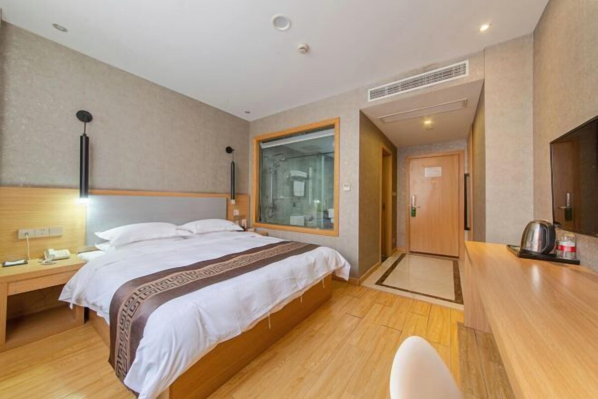 Una camera d'hotel con un letto, un comodino e una piccola scrivania con sedia. C'è un angolo doccia e un angolo cottura completo di forno a microonde e bollitore.