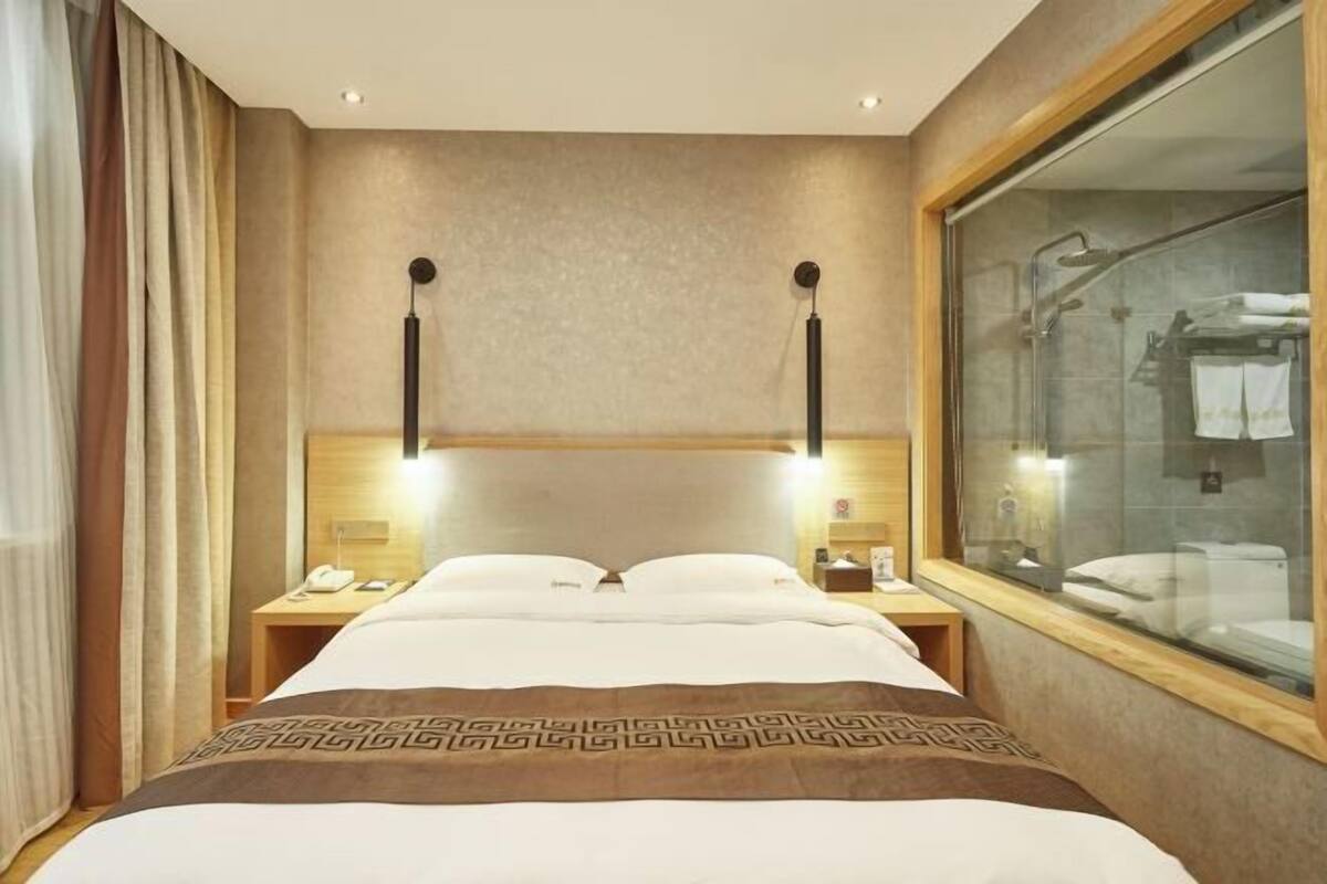 Habitació d'hotel amb un llit gran, taules de nit, una finestra que dona a un bany i una cortina a l'esquerra.