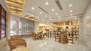 A modern hotel lobby with a central seating area, a reception desk, and a bookshelf.