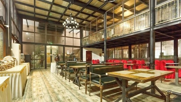 A spacious restaurant with high ceilings, exposed beams, and a mezzanine level. Tables and booths are arranged along the walls, with a wooden floor.