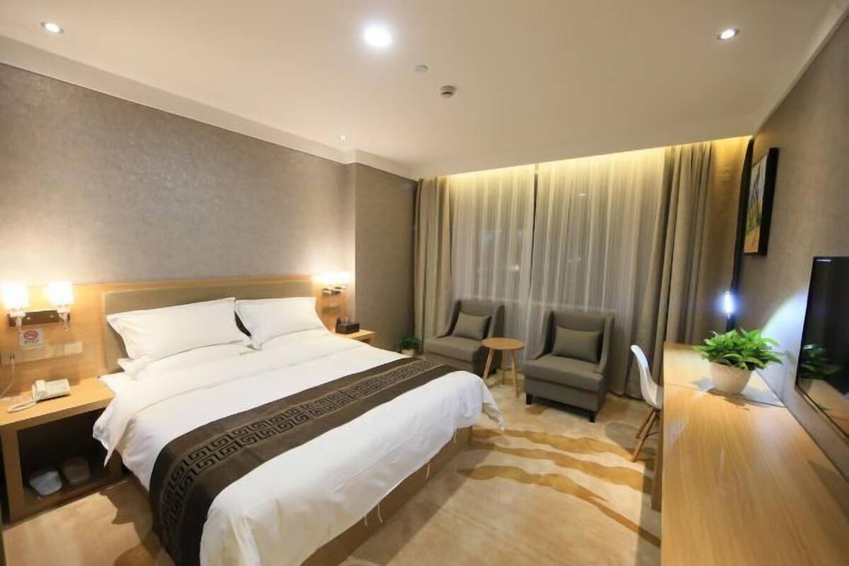 Una habitació d'hotel amb un llit gran, un sofà, una taula petita i una televisió.