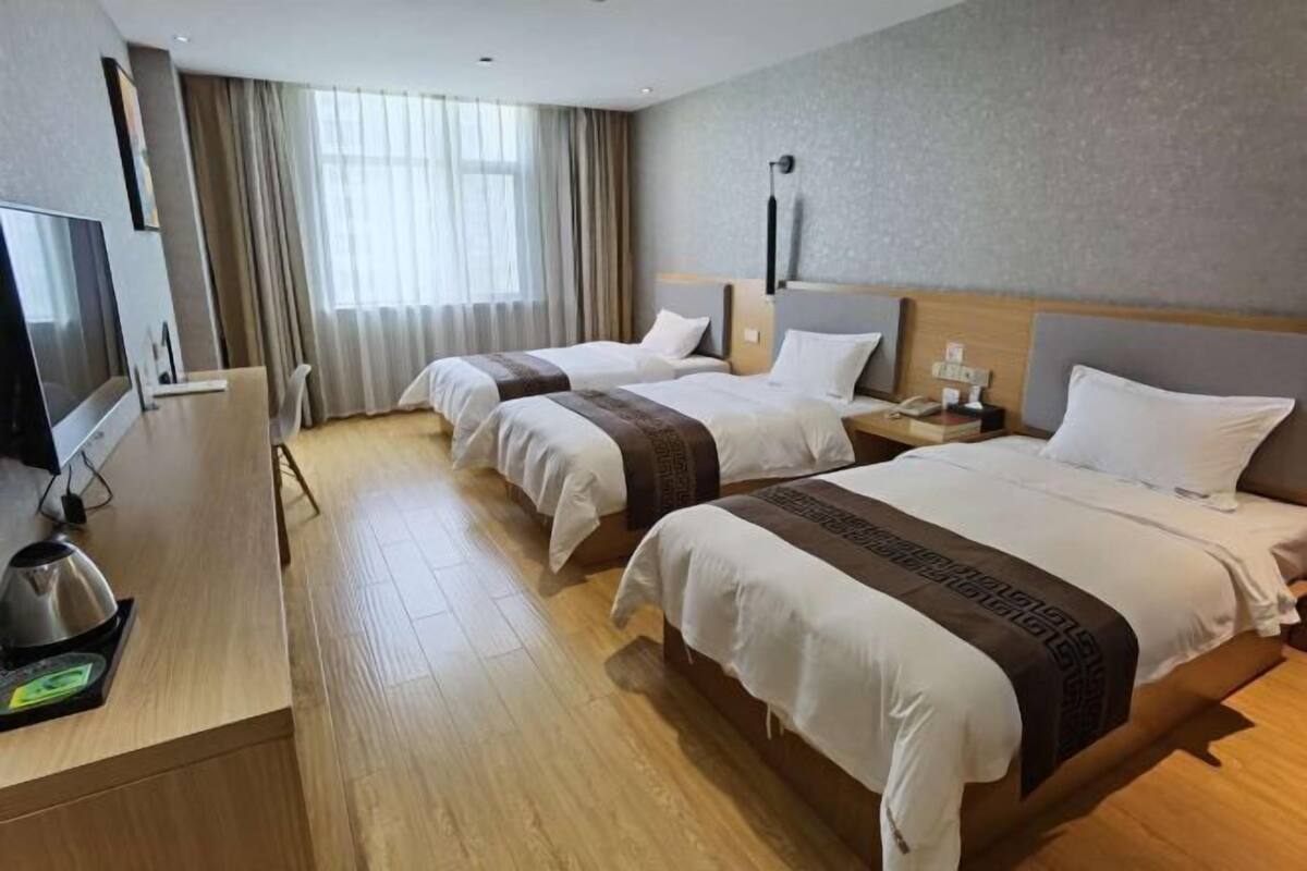 Habitació d'hotel amb dos llits, televisió, escriptori i tetera, i una finestra gran amb cortines.