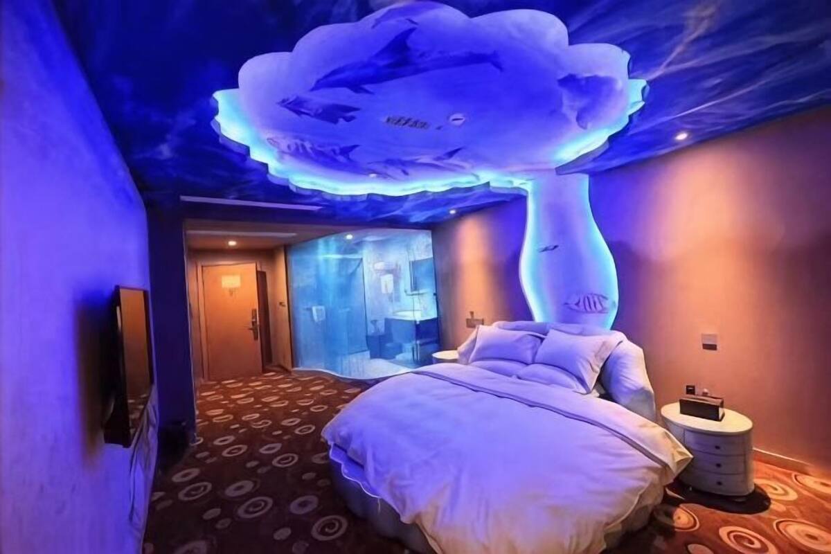 Habitació d'hotel amb llit, tauleta de nit, televisió penjada a la paret i sostre amb un disseny de núvols.