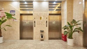 A lobby with two elevators, a trash bin, and potted plants.