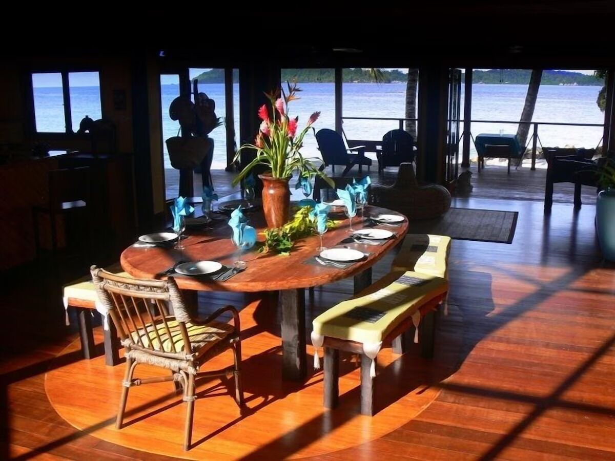 A dining area with a wooden table, chairs, and a view of the sea.