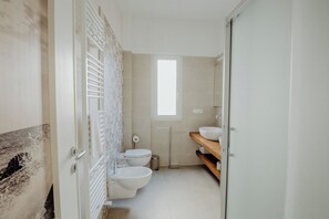 A compact bathroom with a toilet, bidet, and a small window.