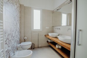 Une salle de bain moderne avec un grand miroir, deux lavabos, des toilettes et des carreaux décorés.
