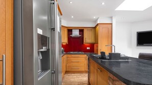 A modern kitchen with wooden cabinets, a stainless steel refrigerator, a black countertop, and a red backsplash.