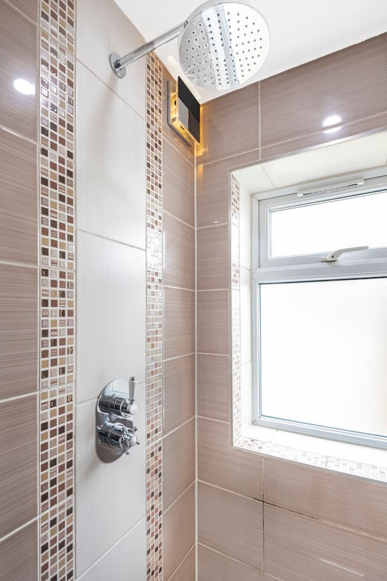 Een douche met regenstortdouche, een raam en betegelde wanden.