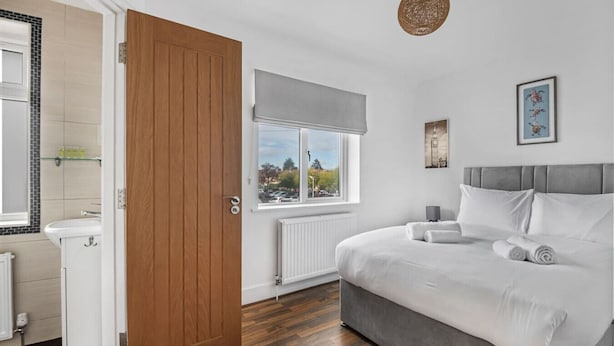 A bedroom with a large bed, a window with a view of the outside, a radiator, and a wooden door.