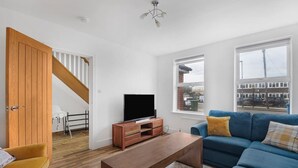 A modern living room with a wooden TV stand, a blue sofa, and a wooden coffee table.