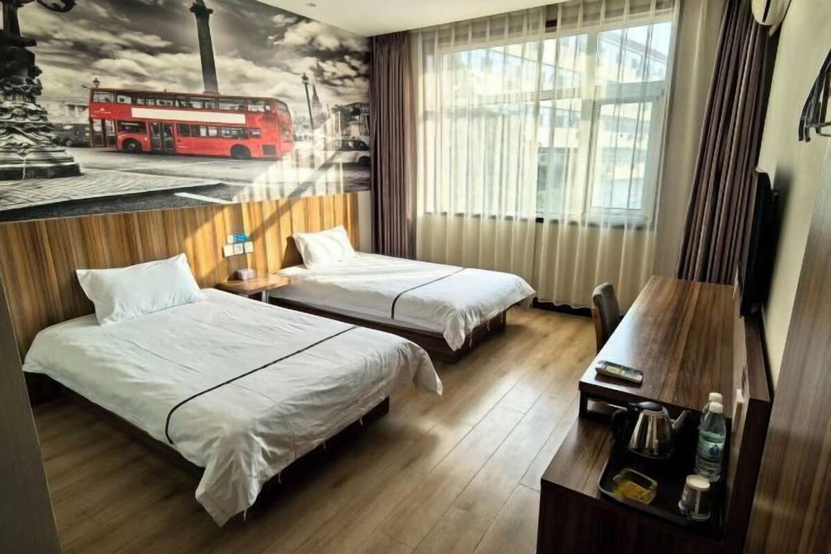 A hotel room with two beds, a wooden desk, a TV, and a mural of a red bus.