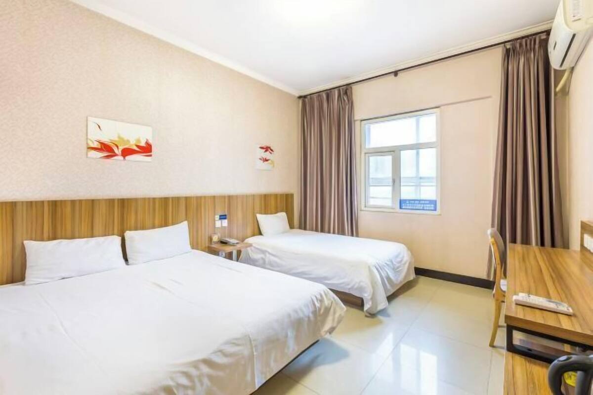 A hotel room with two beds, a wooden headboard, a window with curtains, and a desk with a chair.