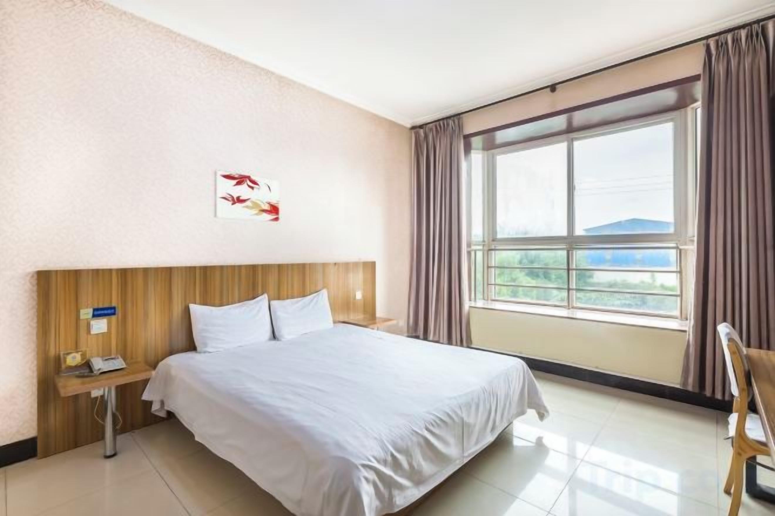 Une chambre d’hôtel avec un grand lit, une table de chevet avec un téléphone et une fenêtre avec des rideaux.