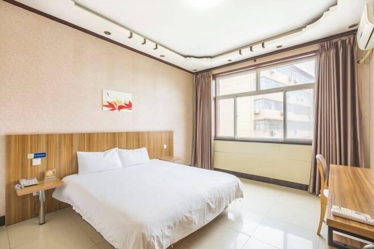 A hotel room with a bed, a desk, a chair, a window with curtains, and a wall-mounted artwork.