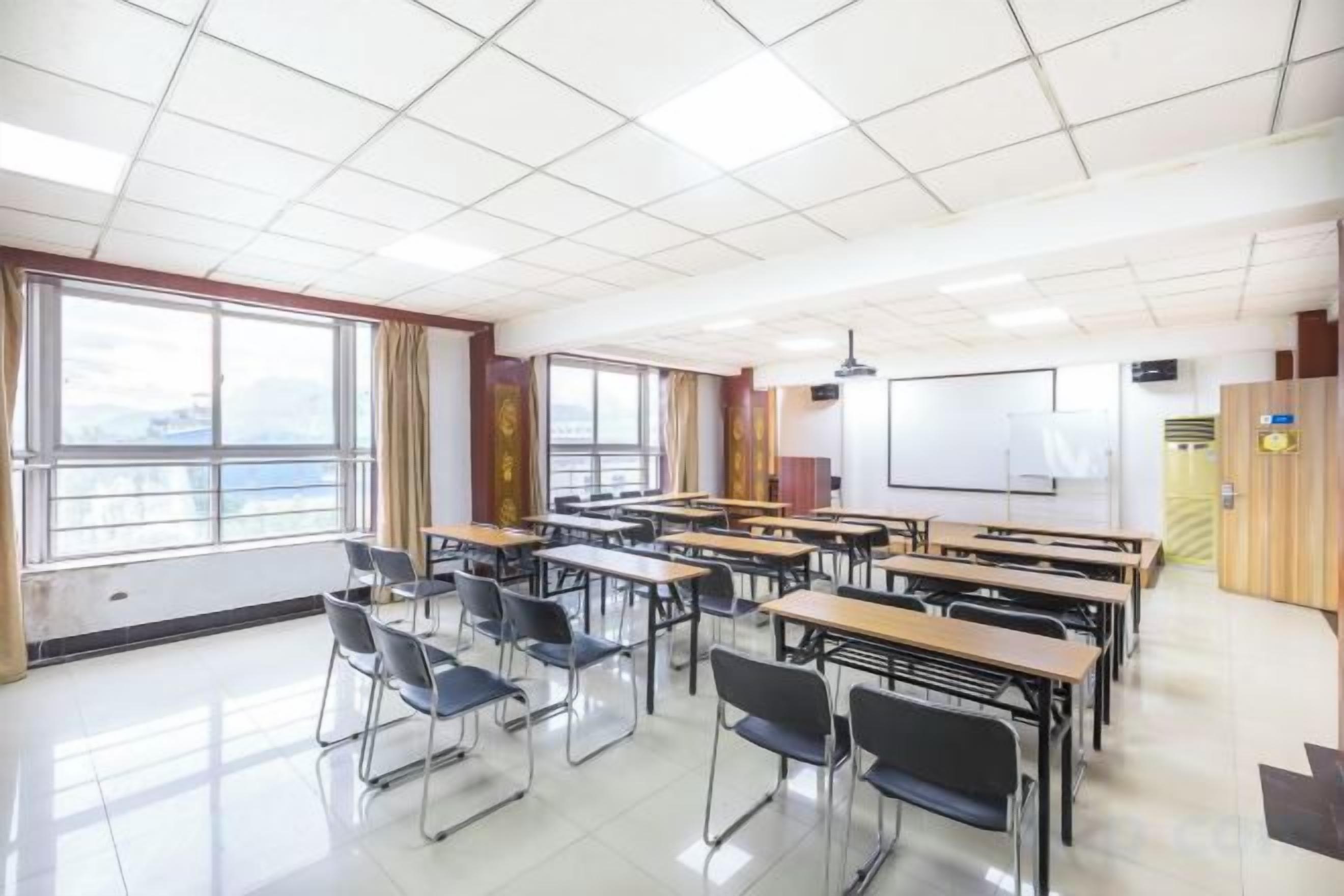 Une salle de classe avec des bureaux disposés en rangées, un tableau blanc et un écran de projection.