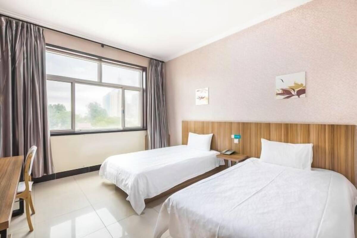 A hotel room with two beds, a wooden headboard, a desk, and a chair.