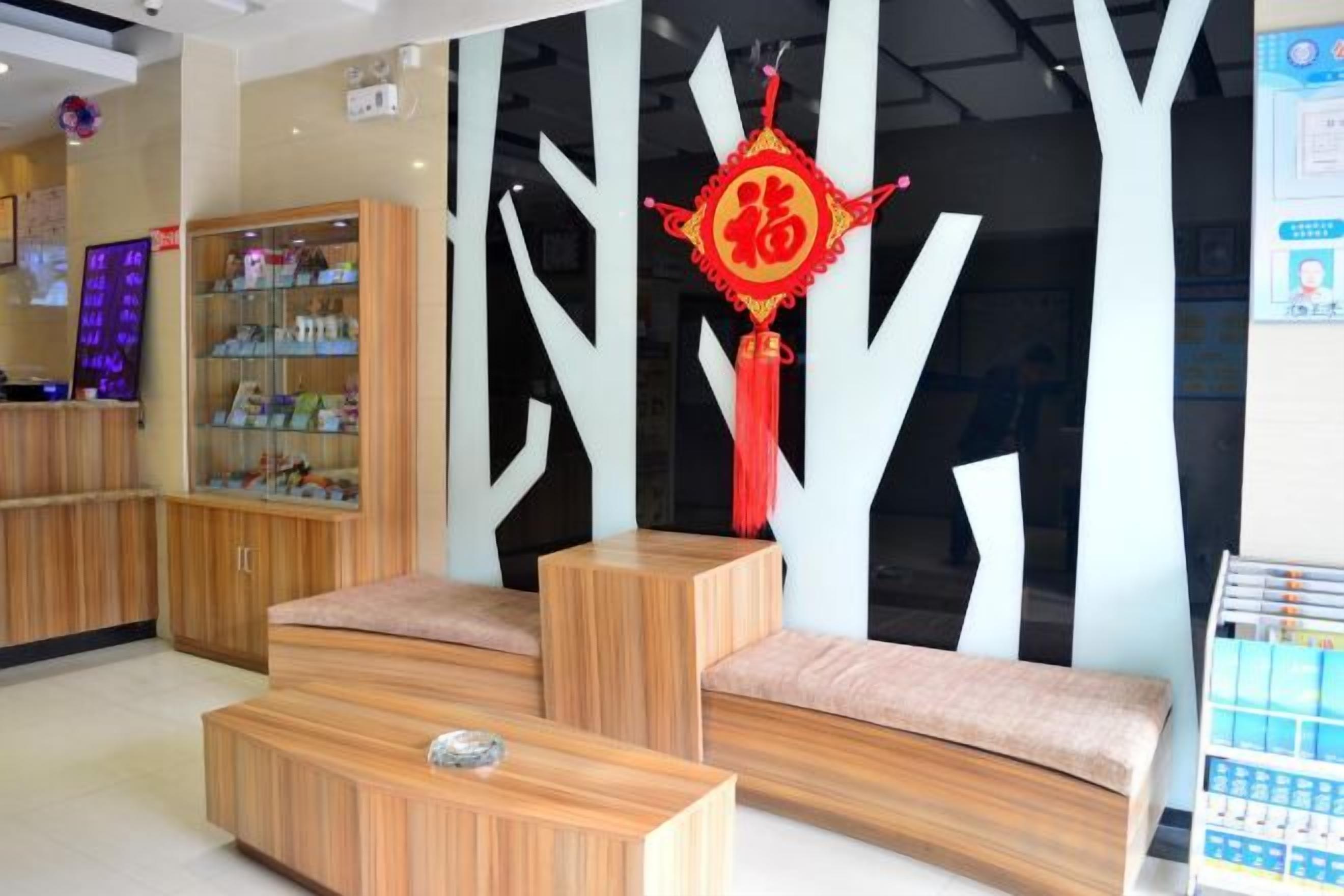 Un espace d’accueil doté d’un comptoir de réception en bois, d’un coin salon avec des bancs rembourrés et d’un mur décoratif agrémenté d’un ornement rouge.