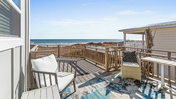 A wooden deck with a white chair and a small table, overlooking the ocean. - Dazzling Oceanfront Condo - Perfect for a Couples Getaway! By Williamson Realty (Ocean Isle Beach)