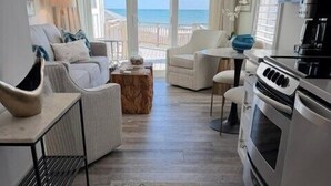 A modern living room with a view of the sea, a kitchen with a stove, and a dining area. - Dazzling Oceanfront Condo - Perfect for a Couples Getaway! By Williamson Realty (Ocean Isle Beach)
