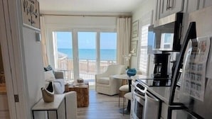 A kitchen with a view of the ocean, a dining area with a table and chairs, and a living area with a sofa and a coffee table. - Dazzling Oceanfront Condo - Perfect for a Couples Getaway! By Williamson Realty (Ocean Isle Beach)