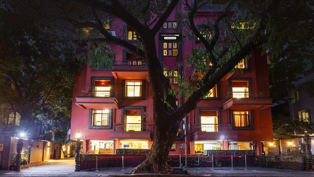 A multi-story building with illuminated windows and a large tree in front. - Deluxe Shivajii Nagar (Pune)
