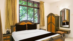 A neatly made bed with a wooden headboard, a bedside table with a lamp, and a large mirror on the wall. - Deluxe Shivajii Nagar (Pune)