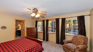 Une chambre à coucher comprenant un lit, une chaise, une commode, un ventilateur de plafond et une fenêtre avec des rideaux.