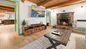 Amplia sala de estar con chimenea de piedra, vigas de madera y un cuadro grande en la pared.