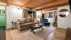 Una sala de estar acogedora con techo de madera, un sofá beige, un sillón azul y una mesita de centro.
