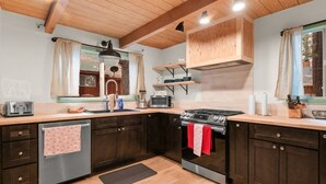 Una cocina con armarios de madera oscura, un lavavajillas de acero inoxidable, una estufa a gas y una ventana con cortinas.