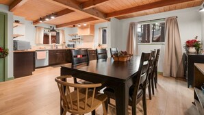 Un comedor amplio con una mesa y sillas de madera, una cocina al fondo y una ventana con cortinas.
