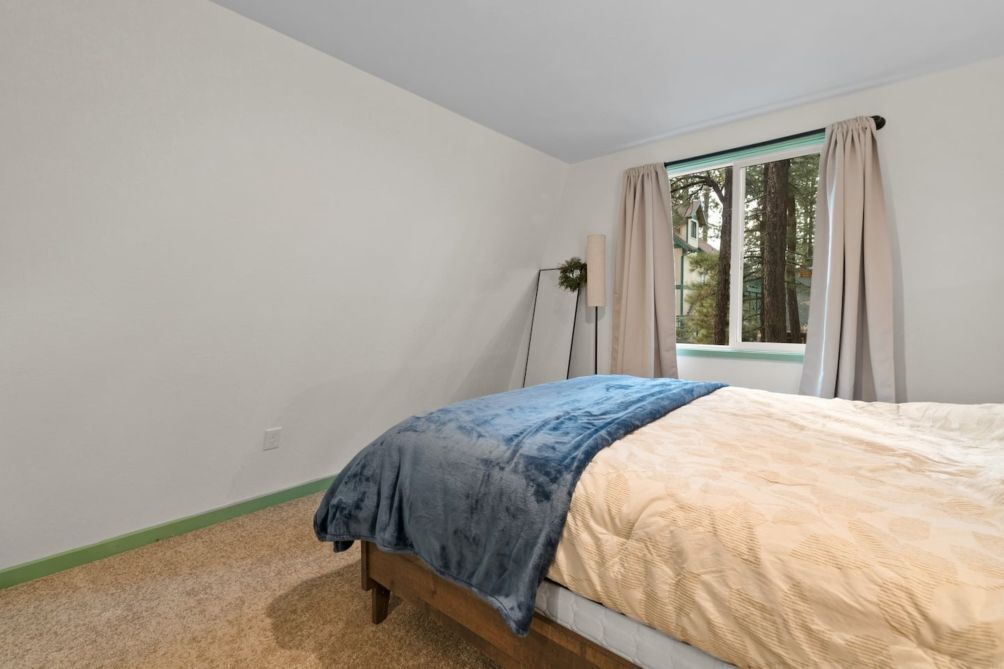 A bedroom with a bed, a window with curtains, a floor lamp, and a view of trees outside.