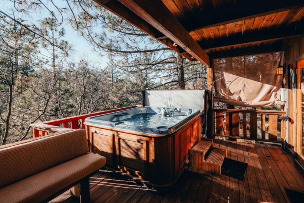 A wooden deck with a hot tub, a bench, and a view of trees.