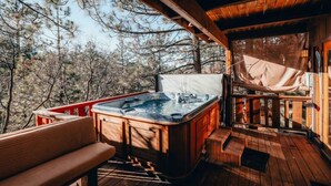 A wooden deck with a hot tub, a bench, and a view of trees. - Moonridge Mountain Retreat (Big Bear)