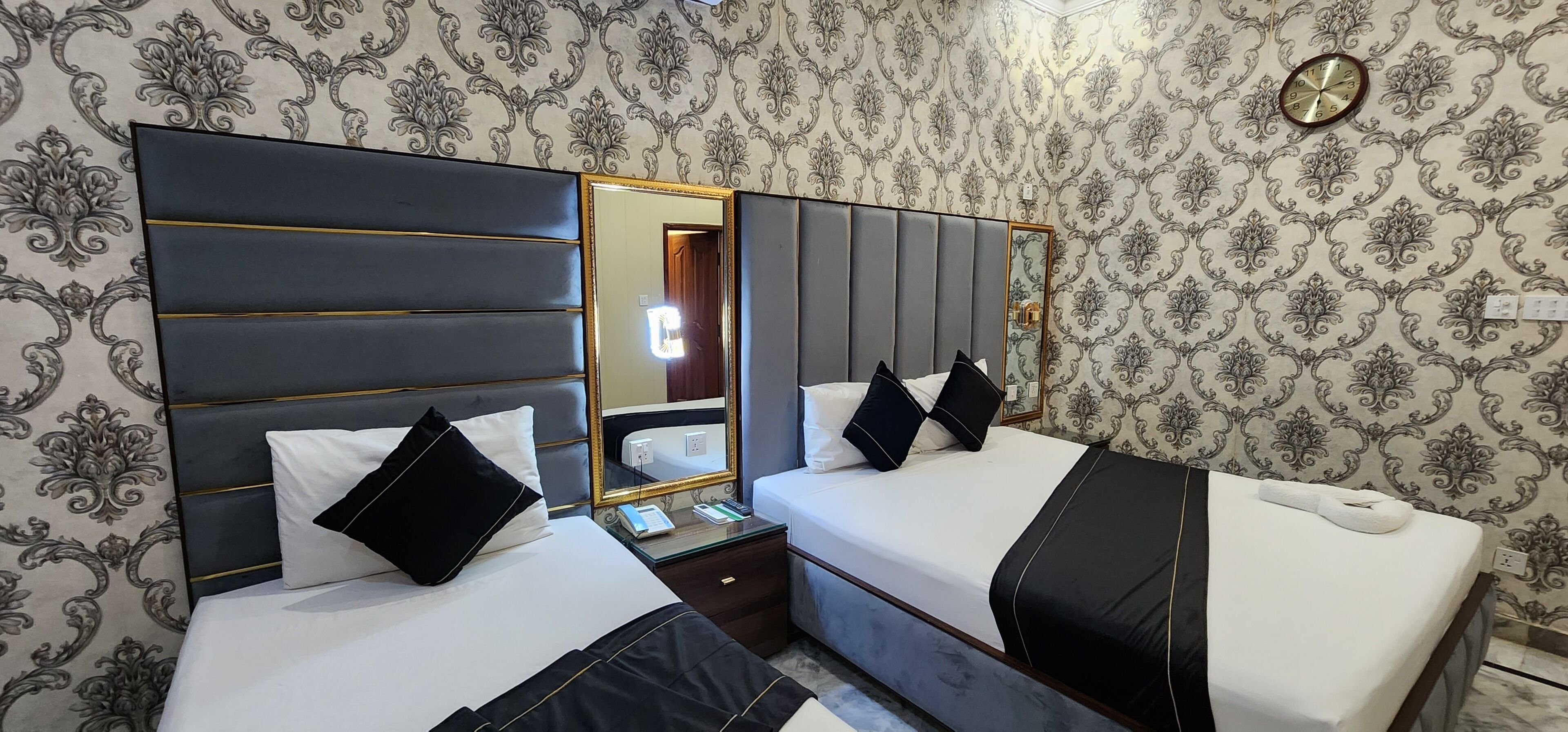 A hotel room with two beds, a large mirror, and a clock on the wall.