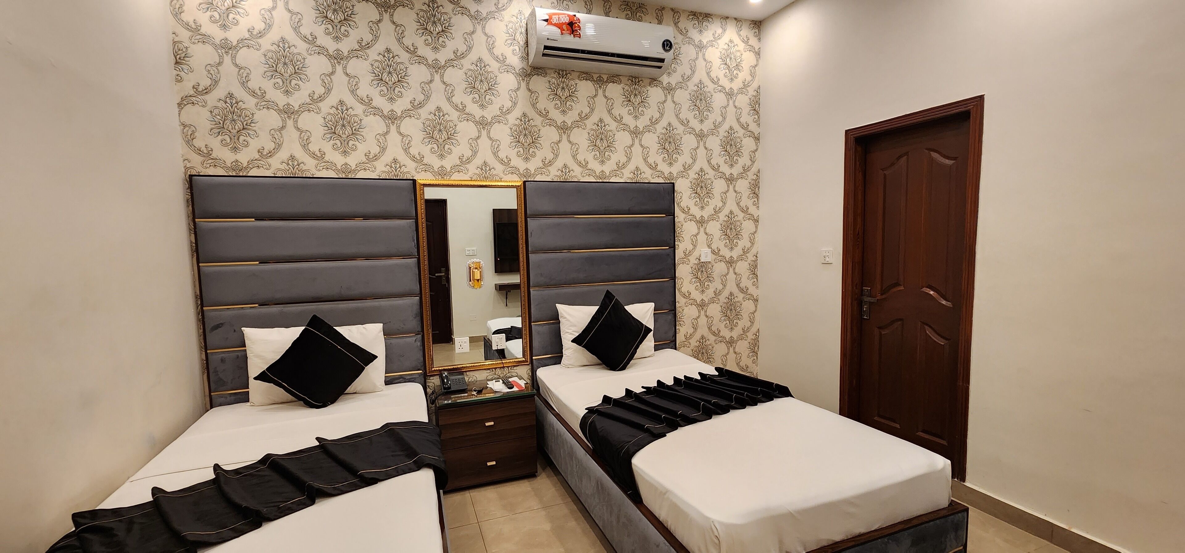 Une chambre d’hôtel avec deux lits, un grand miroir, une porte en bois et un papier peint à motifs.