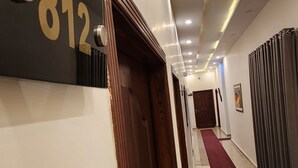 A hotel hallway with a number sign, a wooden door, a red carpet, and a ceiling with recessed lighting. - Red Fort Hotel Gulberg (Lahore)