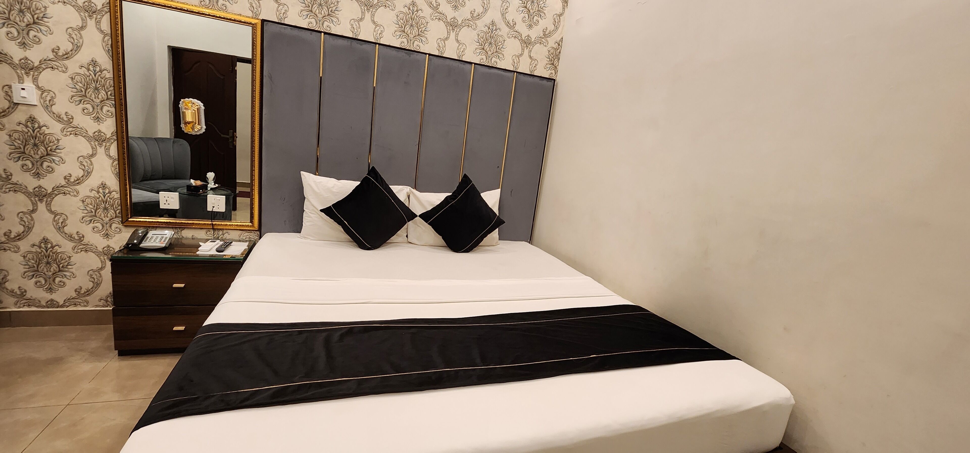 Una cama bien hecha con ropa de cama blanco y negro, una mesita de noche con un teléfono y un espejo en la pared.
