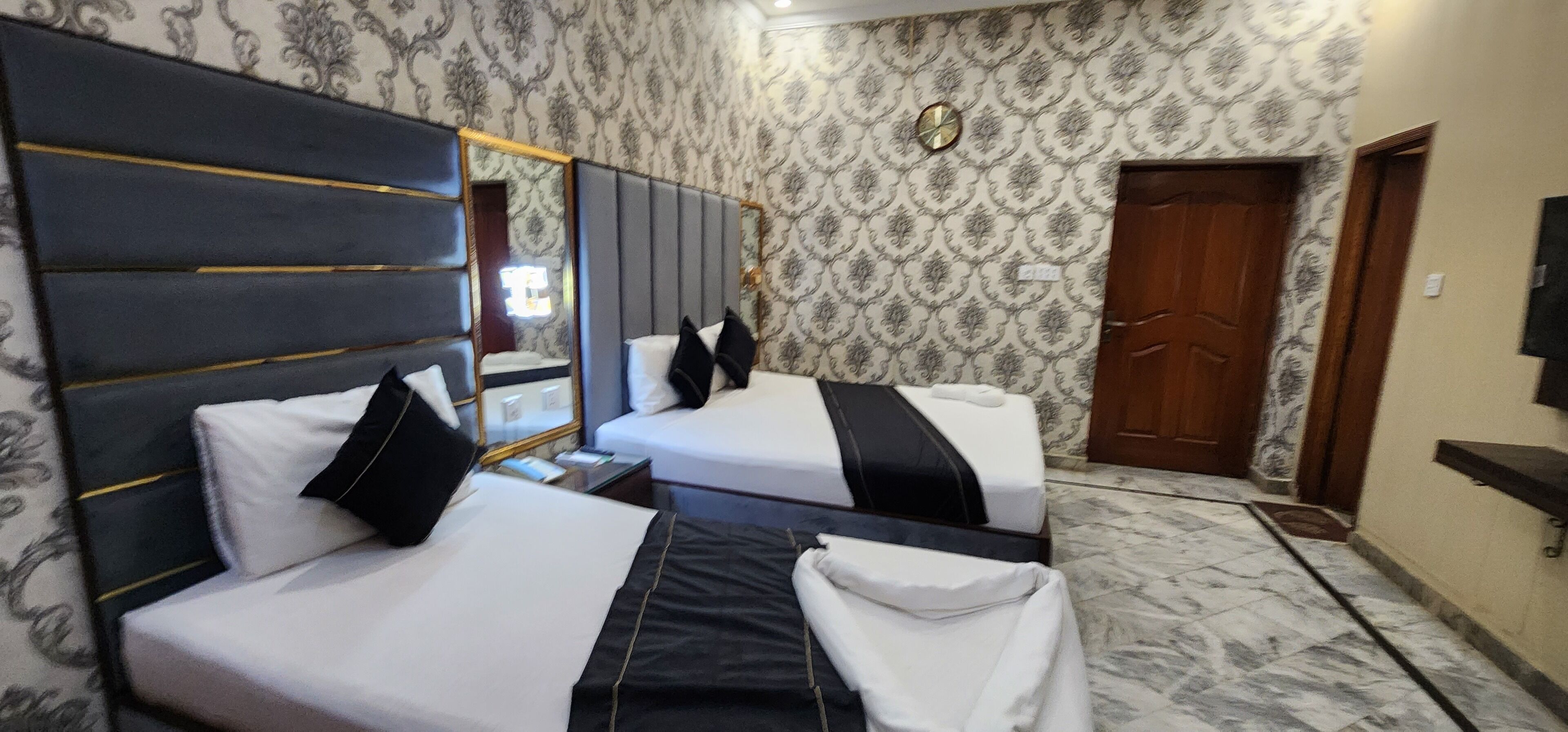 A hotel room with two beds, a large mirror, a clock, and a wooden door.