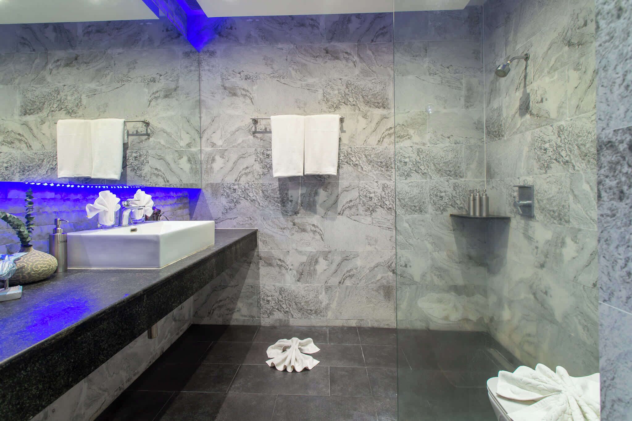A modern bathroom with a marble wall, a white sink, and a shower area.