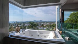A modern bathroom with a large bathtub, a vase, and a view of a cityscape through large windows.