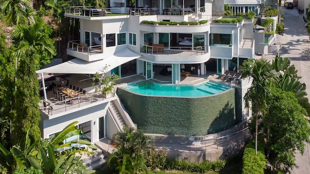 A modern multi-story hotel with a central pool, outdoor seating, and lush greenery.